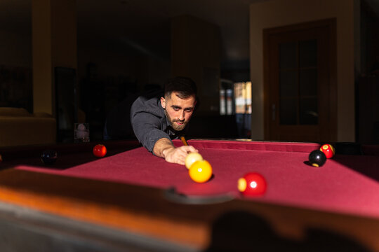 Elegant man playing billiards aiming shot at home