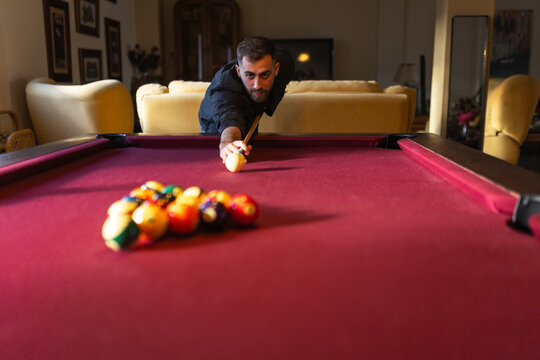 Elegant man playing billiards aiming shot at home
