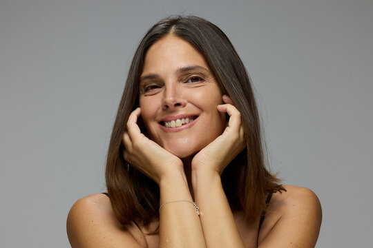 Woman Smiles While Resting Hands on Her Face in Studio Setting