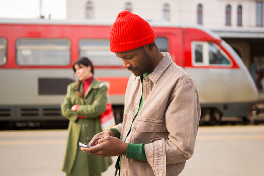 Man Using Phone at Train Station Near Woman Waiting