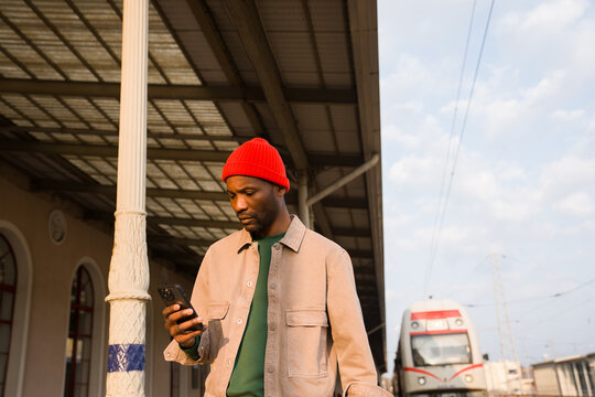 Man Stands at Train Station While Looking at His Phone