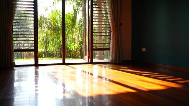 Sunlight streaming through open doors into an empty room with polished wooden floors and a view of a lush tropical garden