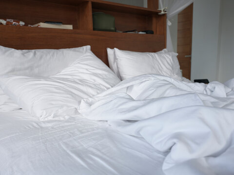Messy Bed With White Sheets and Pillows in a Simple Room Setting