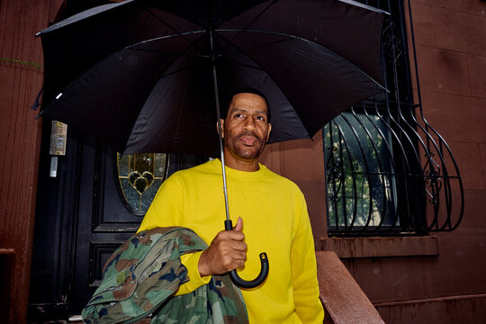 Man stands in front of a house in Brooklyn, holding an umbrella