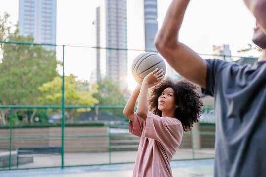 Girl shoots basketball with coach on outdoor court.