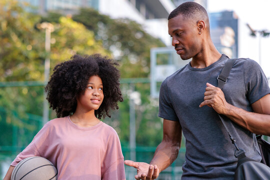 Father and daughter on basketball court, sharing a moment.
