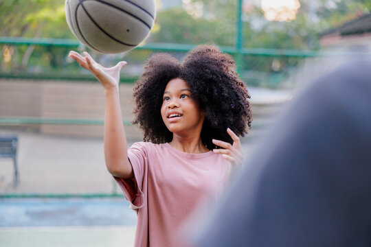 Girl with curly hair tosses basketball on outdoor court.