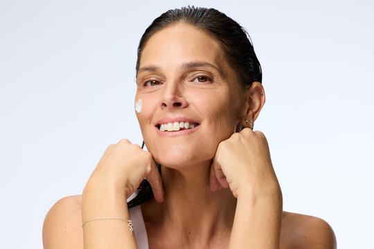 Woman Applying Cream on Her Face During Skincare Routine in Studio