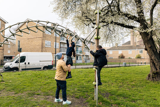 Father helping children playing on school playground monkey bars