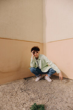 Young Man Squatting in Corner with Sunglasses