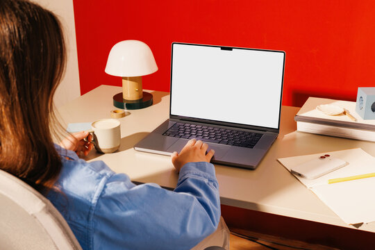 Woman working on laptop with white screen and coffee in office mockup