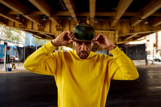 A man in a yellow hoodie stands beneath an overpass.