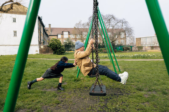 Child pushing parent on school swing in park