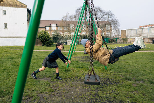 Child pushing parent on school swing in park school playground
