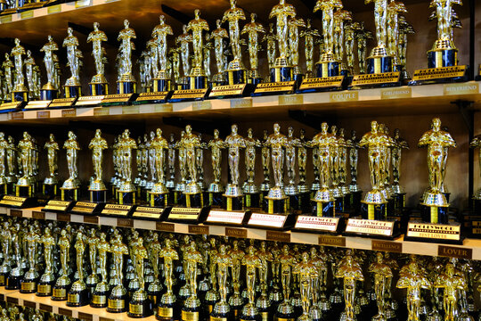 Oscar award trophies on wooden shelves in tight rows, a dense collection of shiny film statuettes filling a showroom display