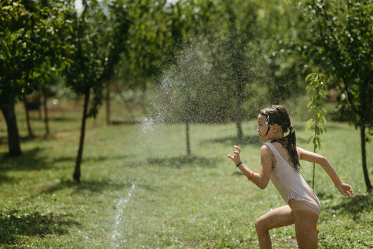 Happy Girl Running and Playing with Water in Sunny Backyard