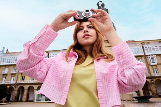 Woman holding compact camera photographing city square