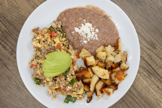 Overhead view of breakfast machaca huevos egss complete with potatoes and beans garnished with avocado. 
