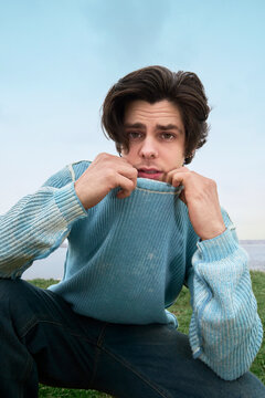 Man sitting outdoors pulling sweater collar over face