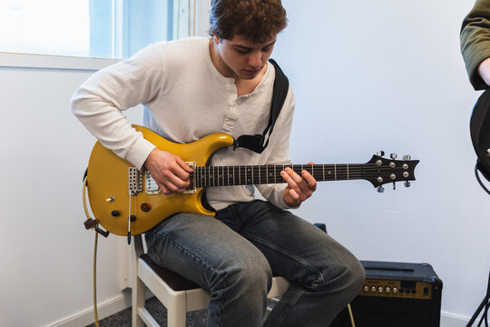 Young student playing gold electric guitar in studio