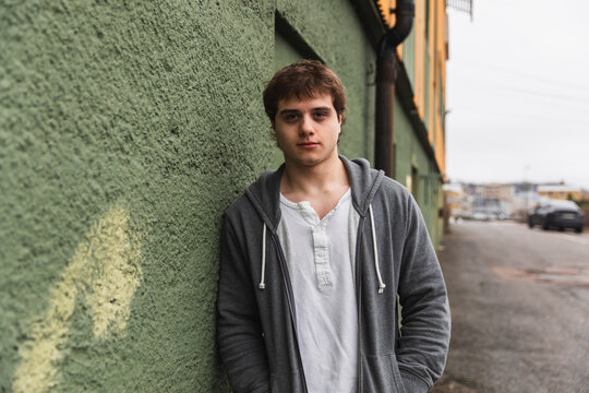 Authentic Young Man in Casual Hoodie Leaning on Textured City Wall