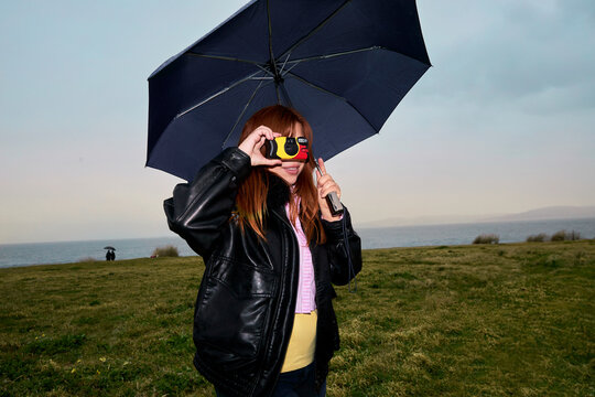 Woman holding umbrella and camera near coastal landscape
