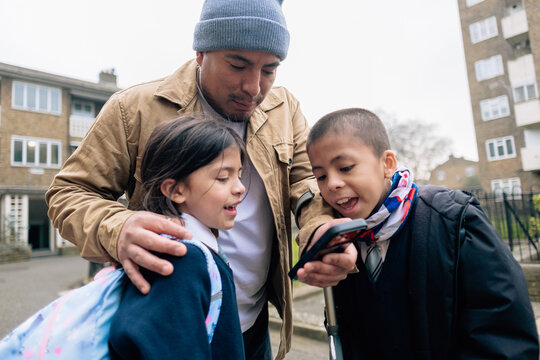 Father picking up children from school using phone