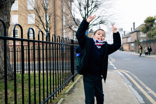 Cheerful schoolboy making peace sign on sidewalk