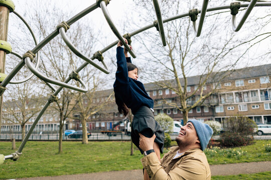 Father helping daughter playing on playground monkey bars