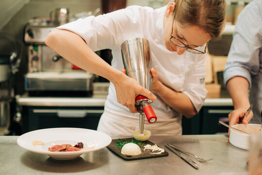 Chef using cream siphon for gourmet dish preparation