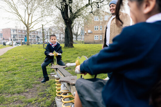 Father cheerfully watching children playing on seesaw