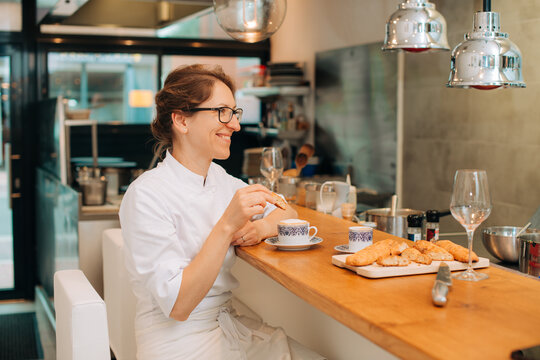 Female chef enjoying pastry and coffee at kitchen counter
