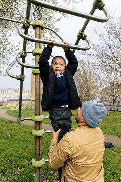 Parent helping joyful child playing on monkey bars