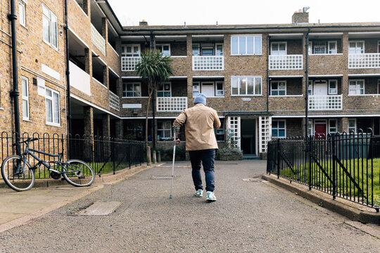 Individual with crutch walking towards social housing building