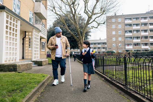 Father with crutch walking daughter from school