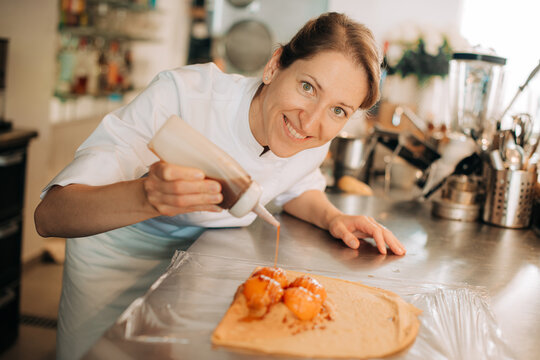 Smiling chef drizzling sauce over apricot crepe dessert