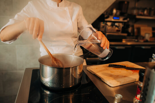 Chef pouring water into pot while cooking on stovetop