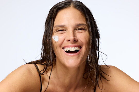 Woman Smiling While Applying Cream on Her Face at Home