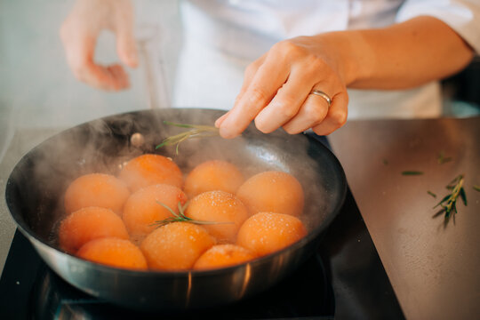 Chef adding herbs to cooking apricots in pan