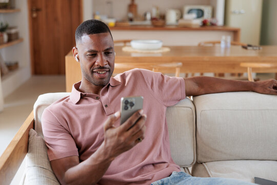 Man on couch using phone with earbuds in.