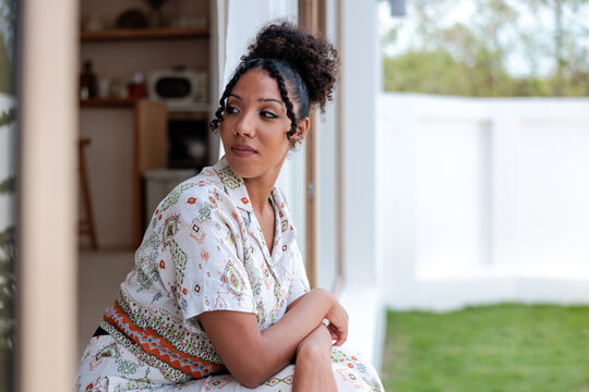 Woman in pajamas looks inside window, thoughtful expression.