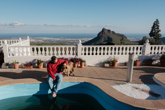 Man and dog relaxing by swimming pool overlooking resort