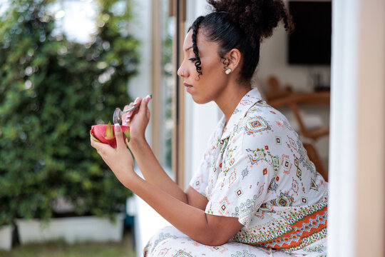Woman eats dragon fruit by window, peaceful moment.