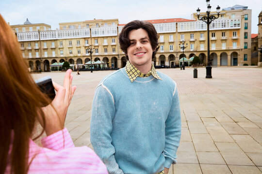 Woman photographing smiling man in historic European city square