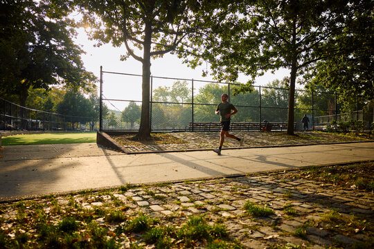 Runner Jogs Along the Park Path in the Morning Sunlight.