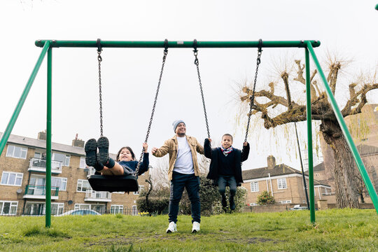 Father playing with children on swings at playground