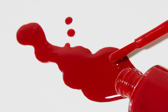 Red nail polish spilling from bottle with brush