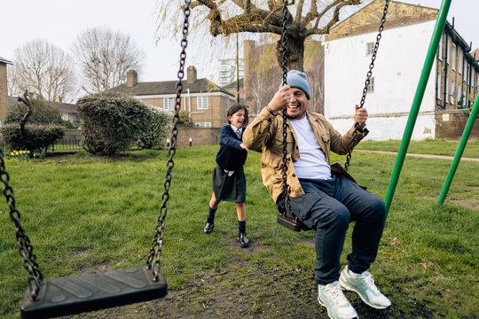 Child pushing parent on school swing in park school playground