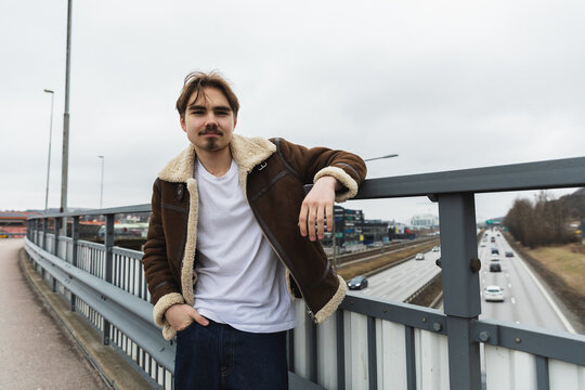 Young man smiling and leaning on a highway bridge railing