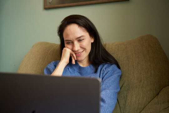 Woman watching laptop screen in armchair